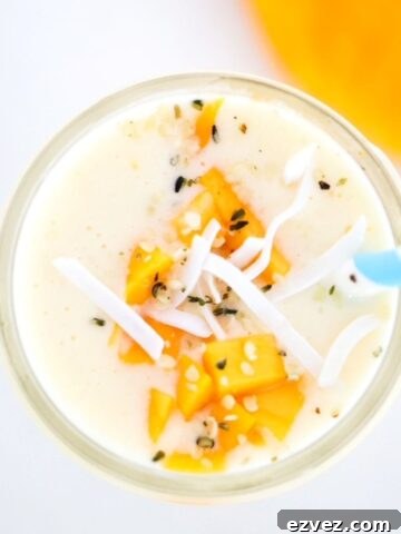 Creamy Mango Pineapple Smoothie topped with mango and coconut flakes with a blue and white striped straw.