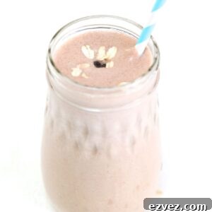 One Peanut Butter Banana Oatmeal Smoothie in a glass jar topped with oats and a mini chocolate chip, served with a straw.