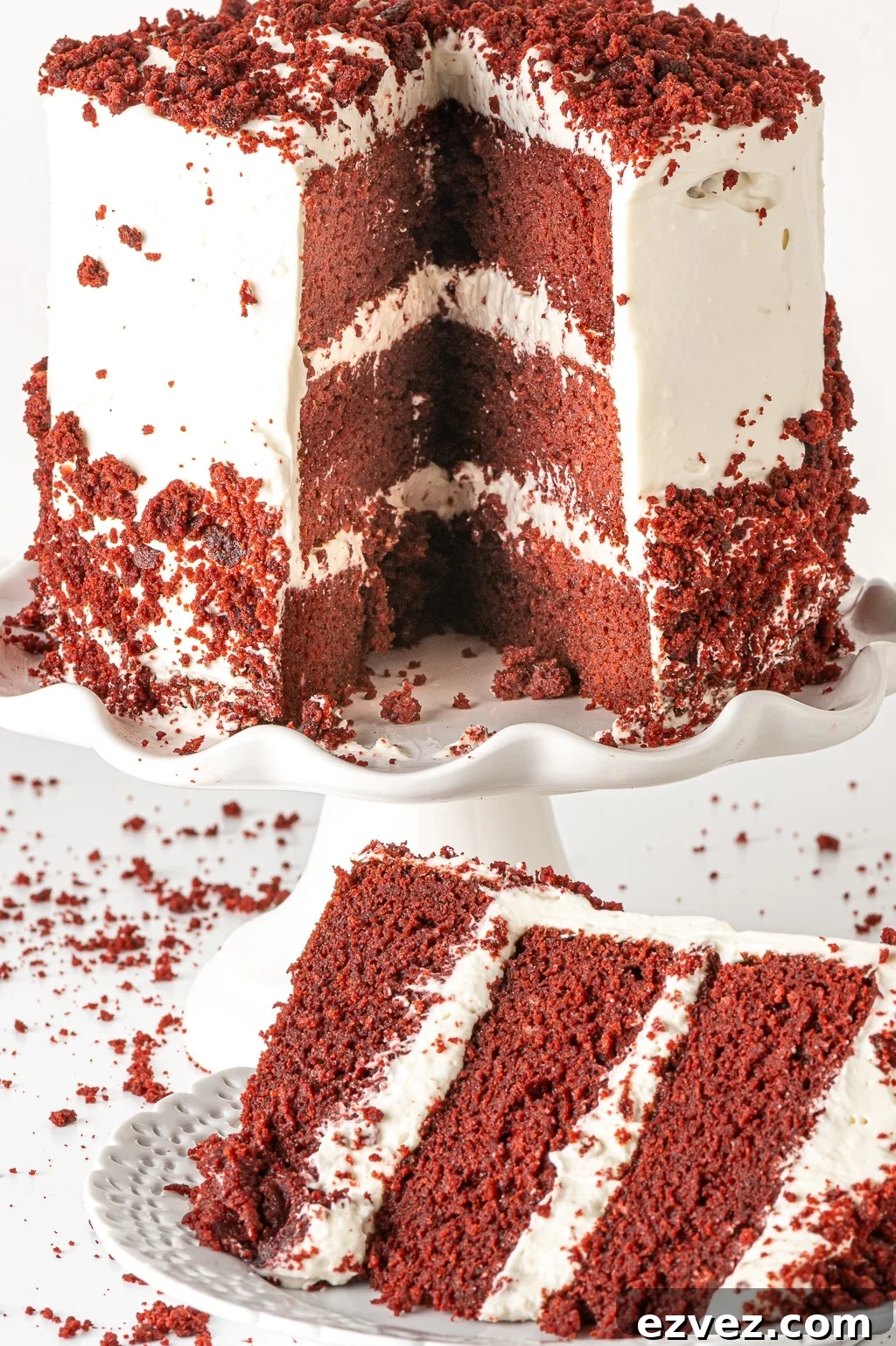 A 3-layer red-velvet cake, coated in creamy white frosting and  cake crumbs. A slice has been taken out and is sitting on a plate ready to be enjoyed.