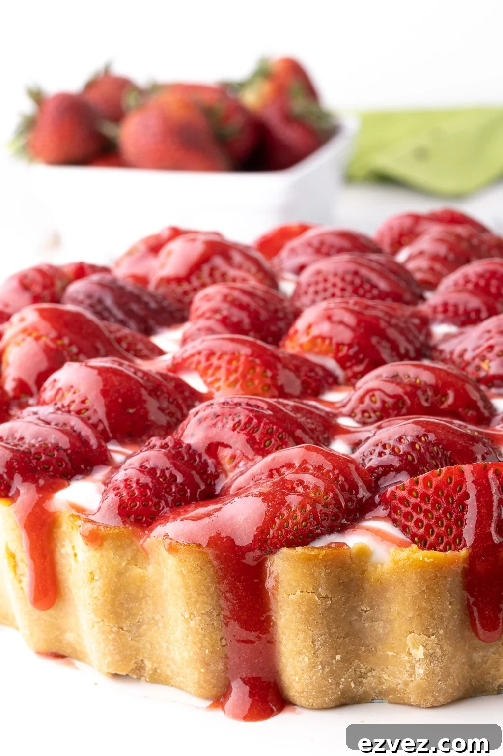 Closeup of a keto strawberry cheesecake, topped with fresh strawberries and strawberry syrup dripping down the sides of the almond crust.