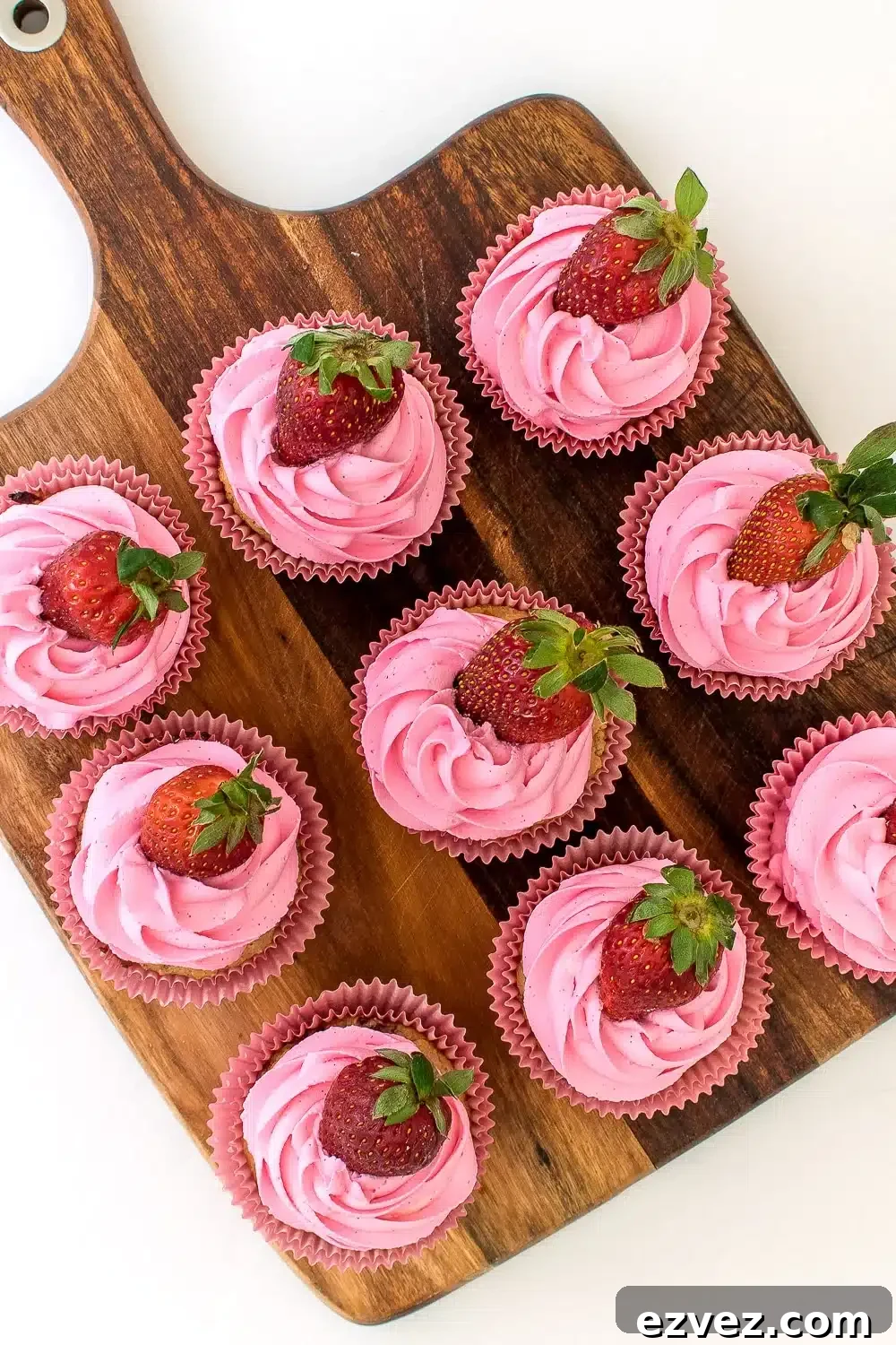 Top view of a batch of pink frosted strawberry cupcakes, each topped with a fresh strawberry.
