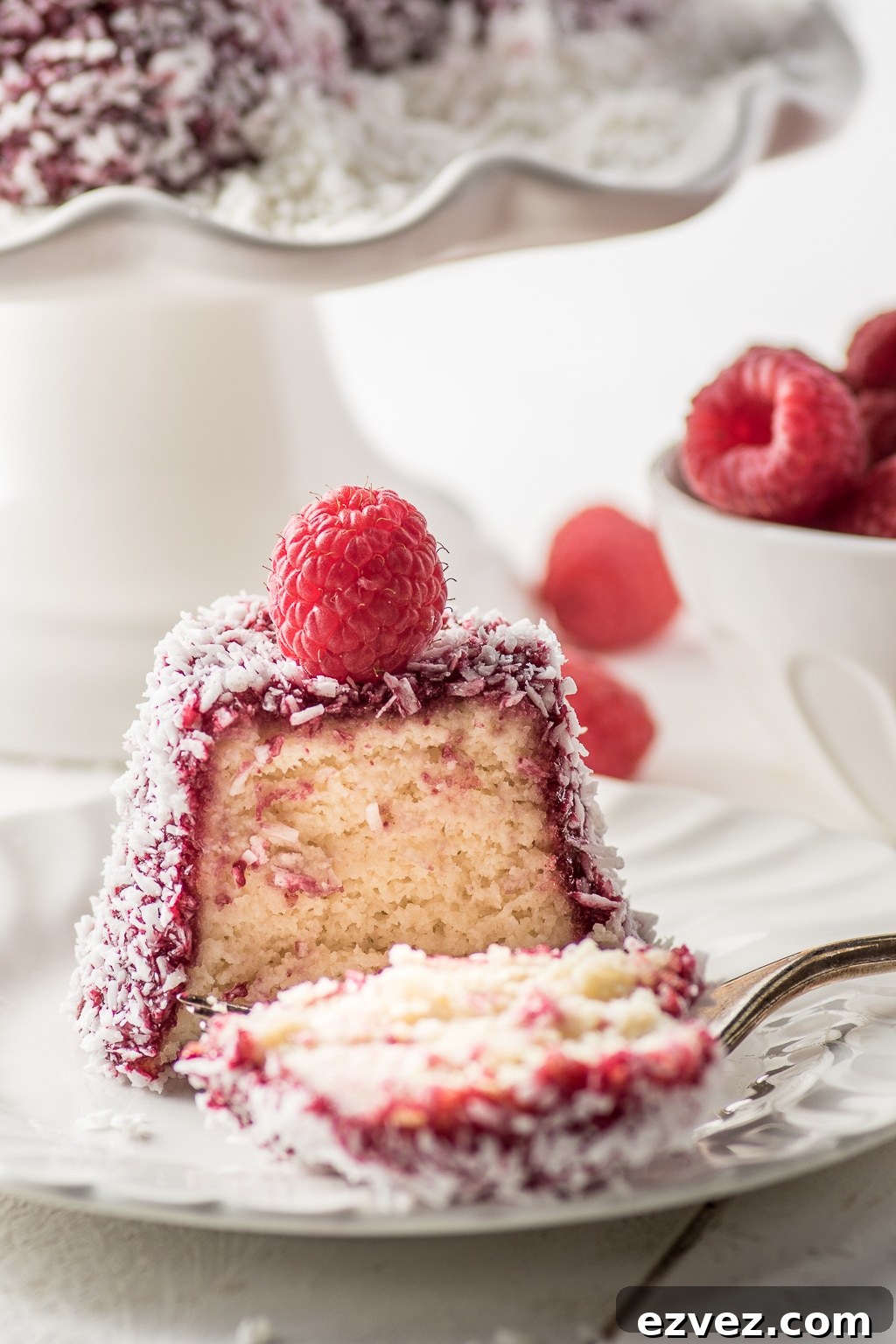 An english madeline, coated with bright red raspberry jam and coconut flakes, with a fresh raspberry on top. A perfect keto dessert for Valentine's day.
