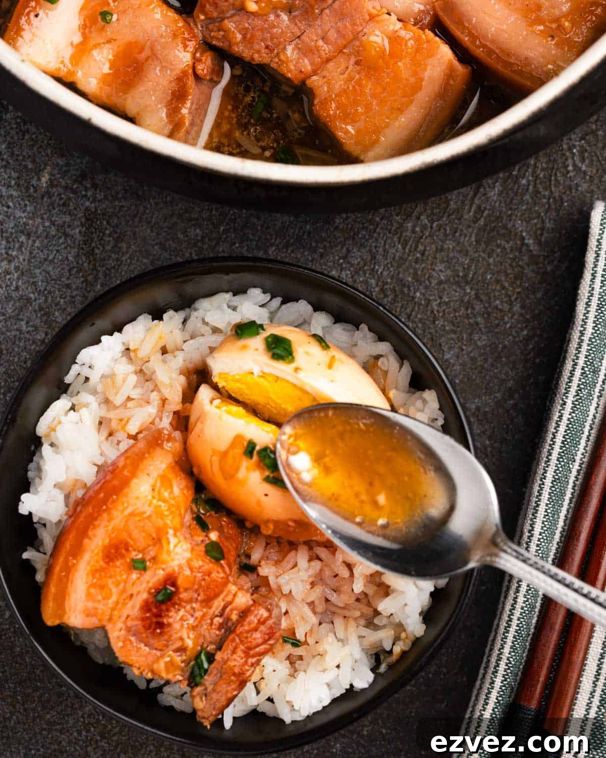 bowl of rice with braised pork belly and eggs with spoon pouring on sauce.