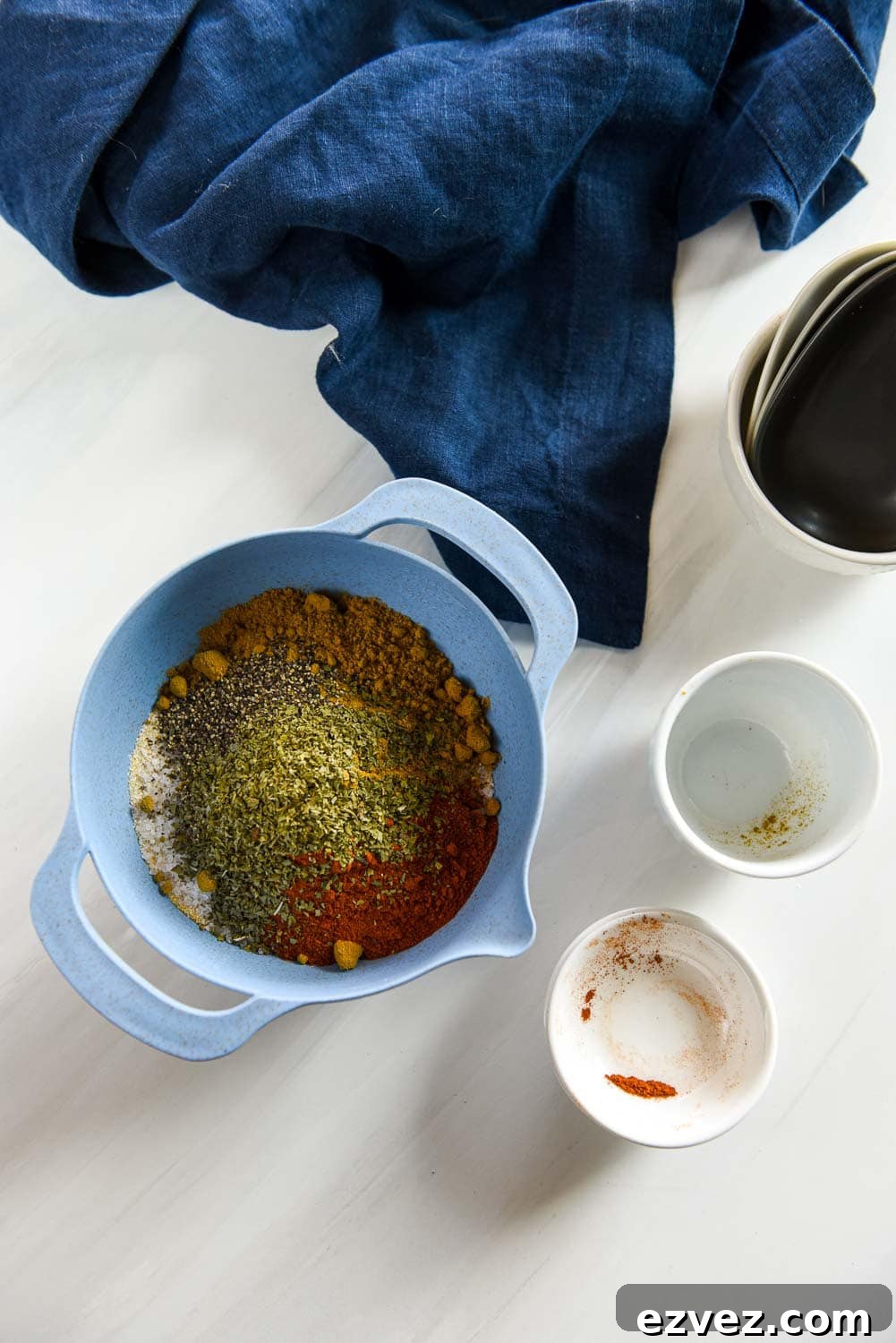 spices in a blue mixing bowl next to empty ramekins