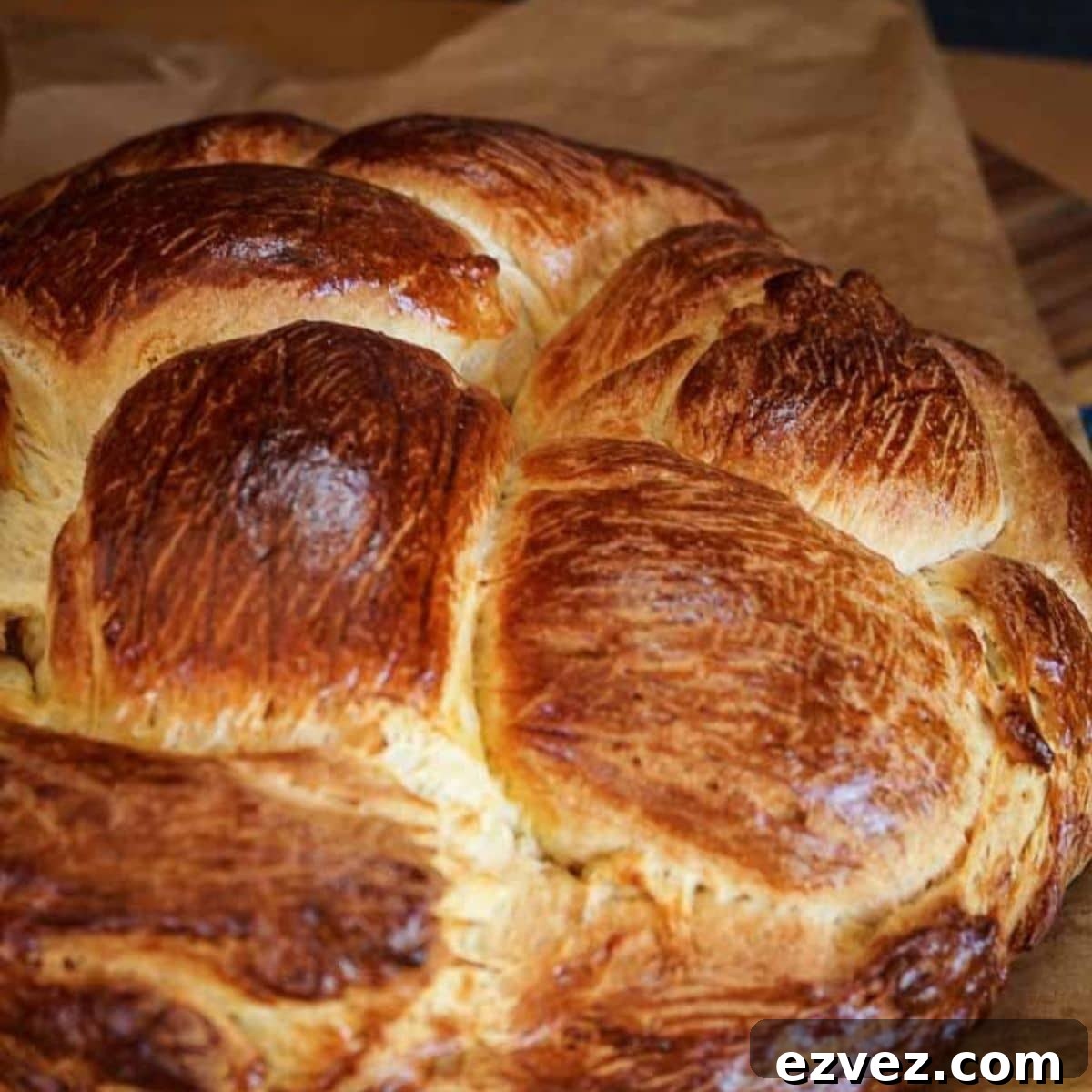 A close up of a loaf of a golden brown round loaf of Hungarian Egg Twist Bread sitting on a piece of parchment paper. Hostess At Heart