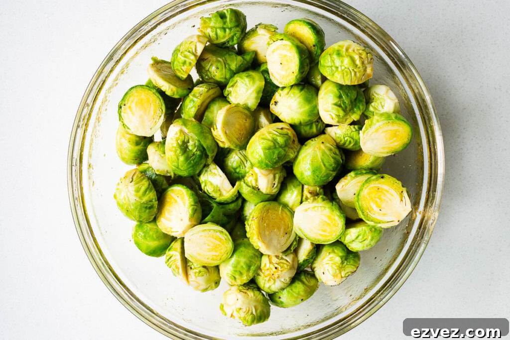 Halved Brussels sprouts coated in honey sauce in a large glass mixing bowl.