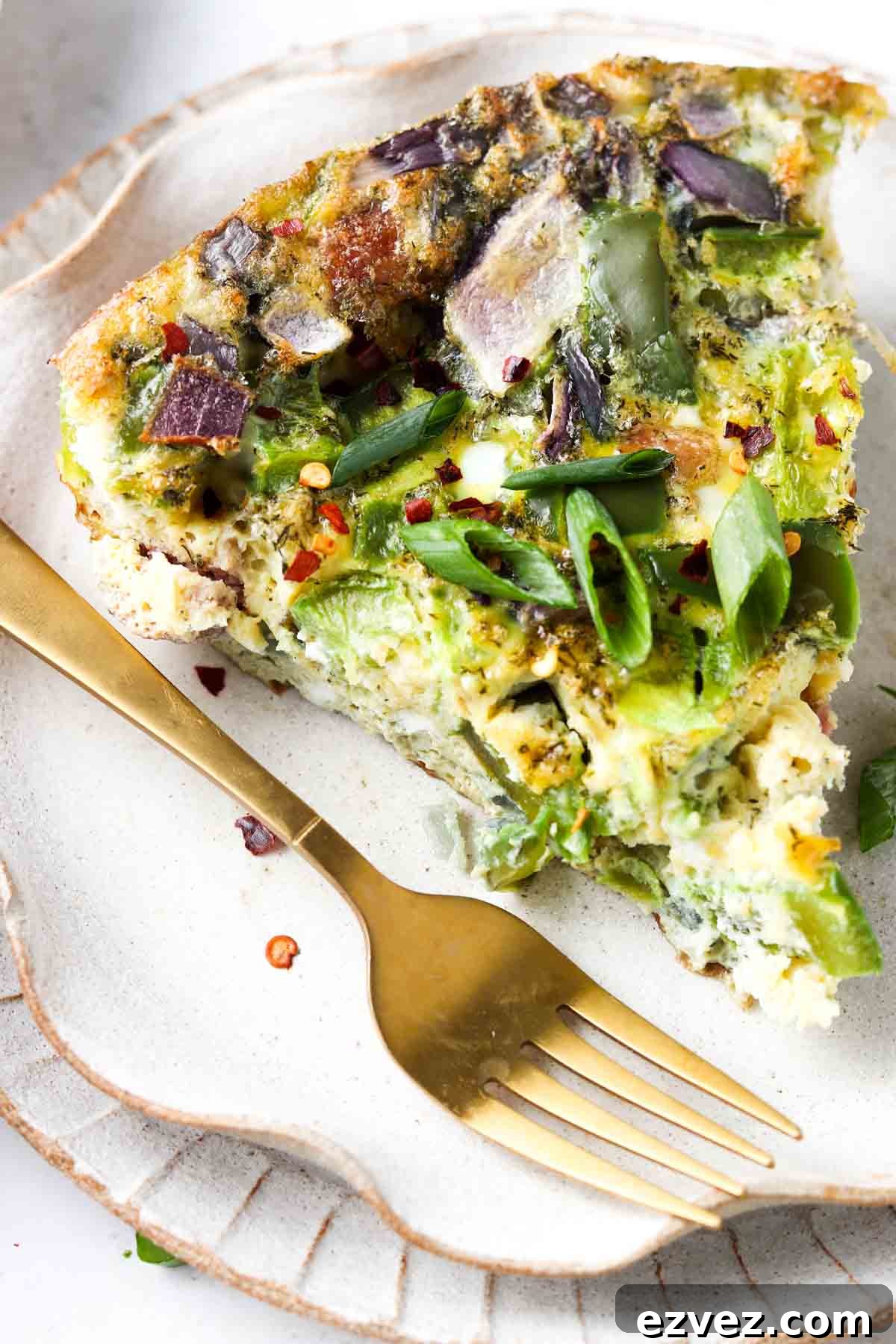 An egg frittata slice on a plate with a gold fork on top.
