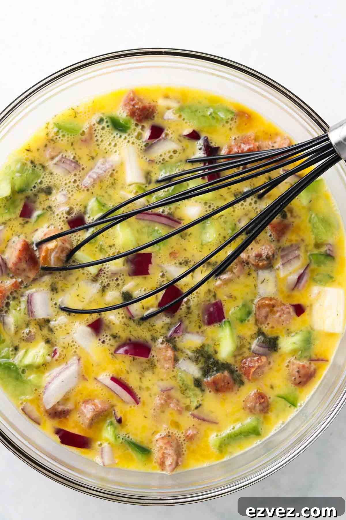 Eggs, peppers, onions and sausage in a glass bowl.