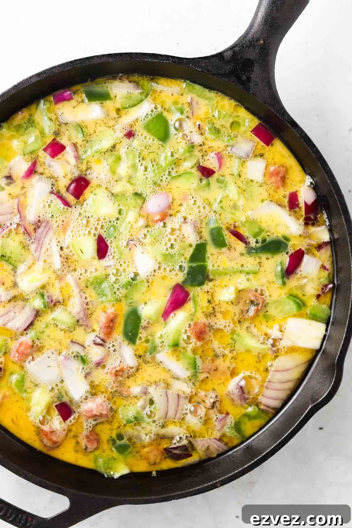 Raw eggs, peppers, sausage and onions in a cast iron pan.