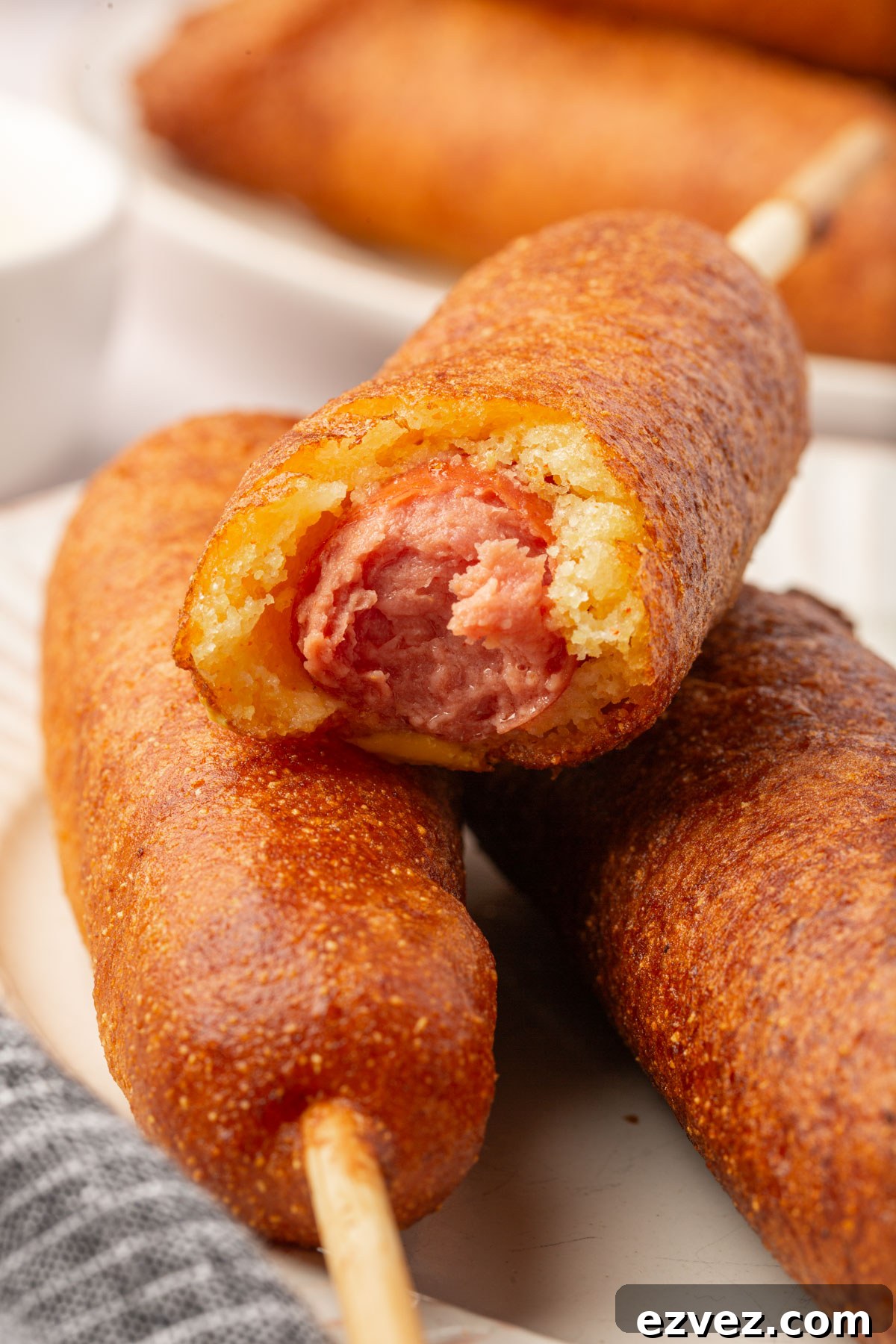 Close-up of stacked gluten-free corn dogs with one bitten to reveal the hot dog inside.