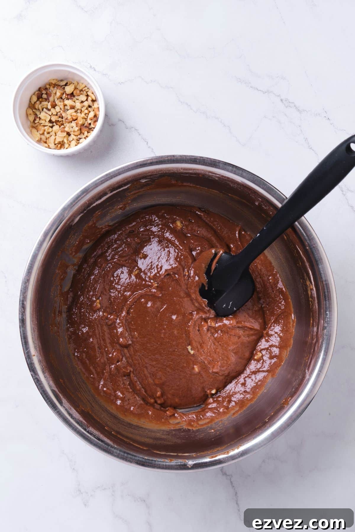 Chocolate cake batter in a bowl with chopped walnuts mixed in.