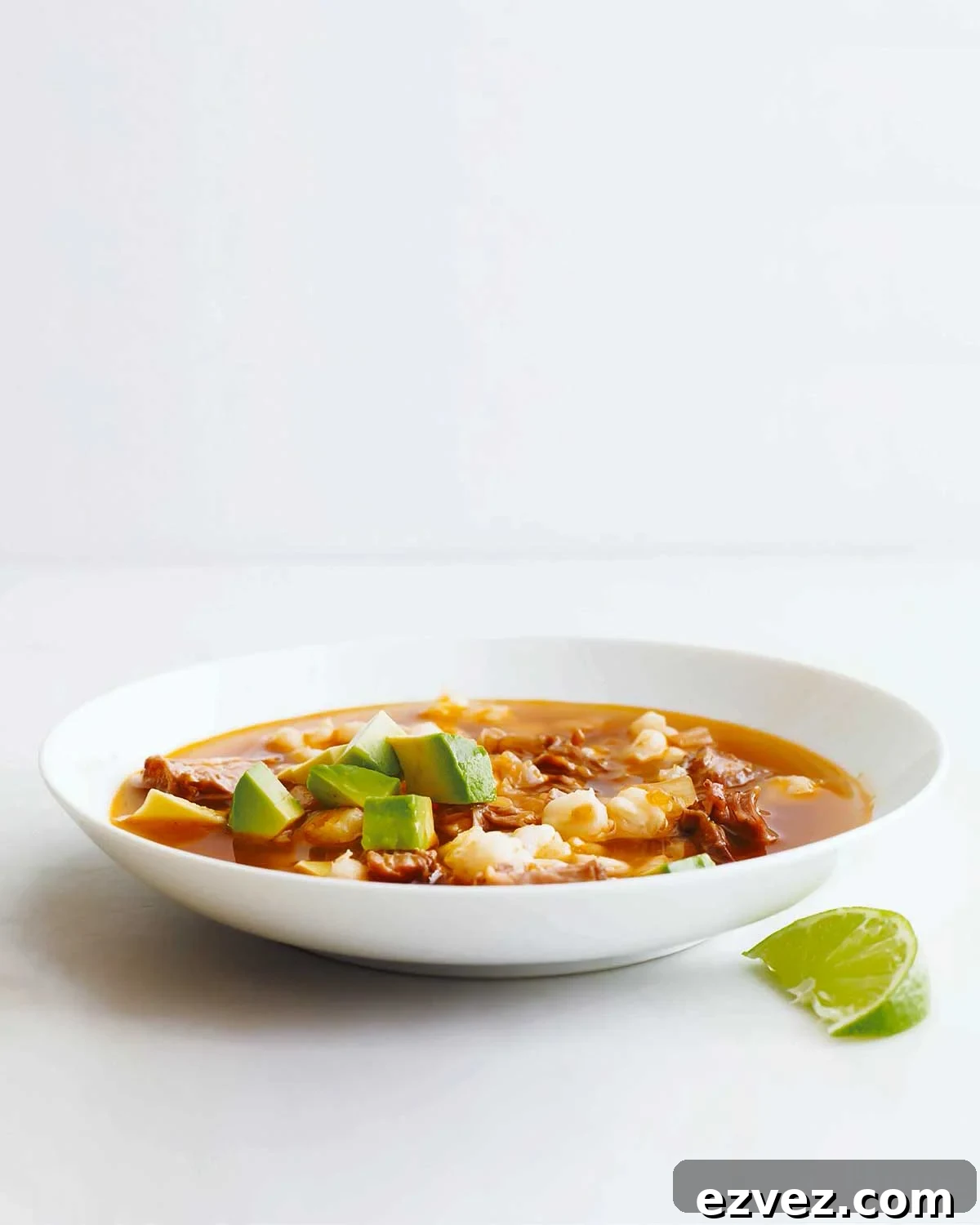 A white bowl filled with quick posole with pork topped with avocado with a lime wedge on the side.