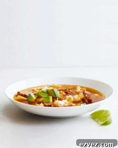 A white bowl filled with quick posole with pork topped with avocado with a lime wedge on the side.