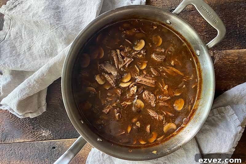 Leftover Pot Roast Mushroom Soup Recipe for Comforting Meals 13 Horizontal image of a dark brown soup with meat and slices of vegetables in a pot.