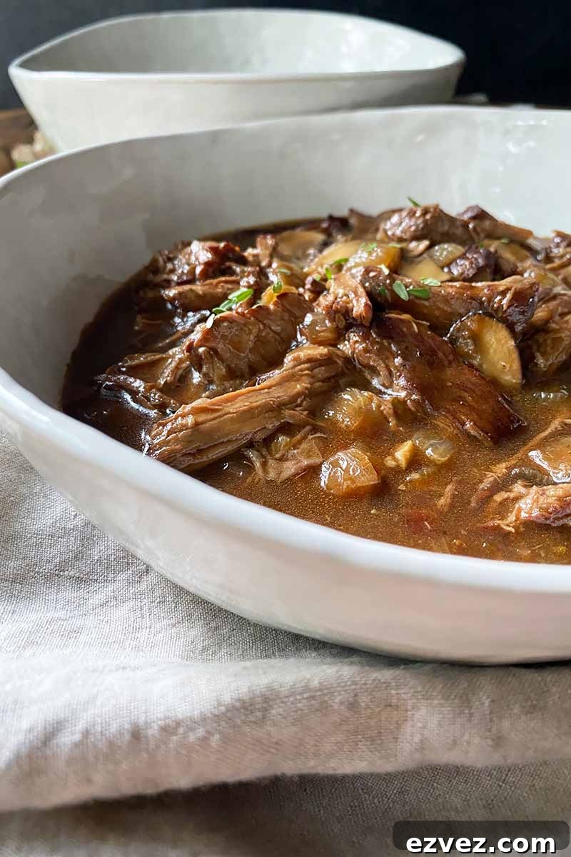 Leftover Pot Roast Mushroom Soup Recipe for Comforting Meals 4 Vertical close-up image of a bowl of dark brown stew on a white napkin.