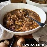 Horizontal image of a white bowl filled with a dark brown chunky stew with a spoon.