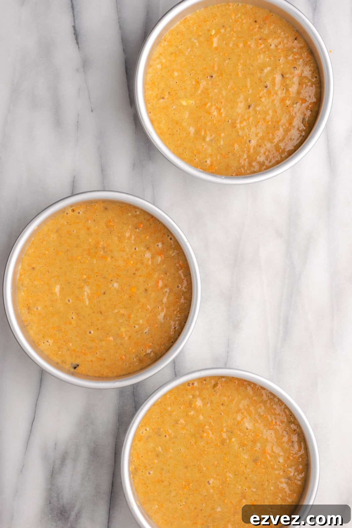 Three round cake pans filled with cake batter.