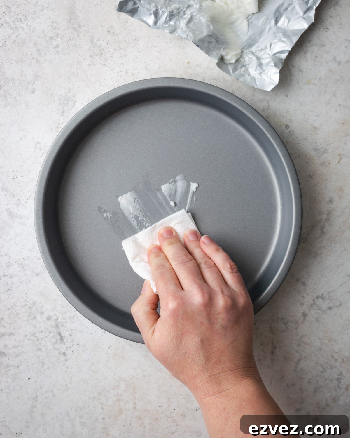 A hand greasing a cake pan with shortening.