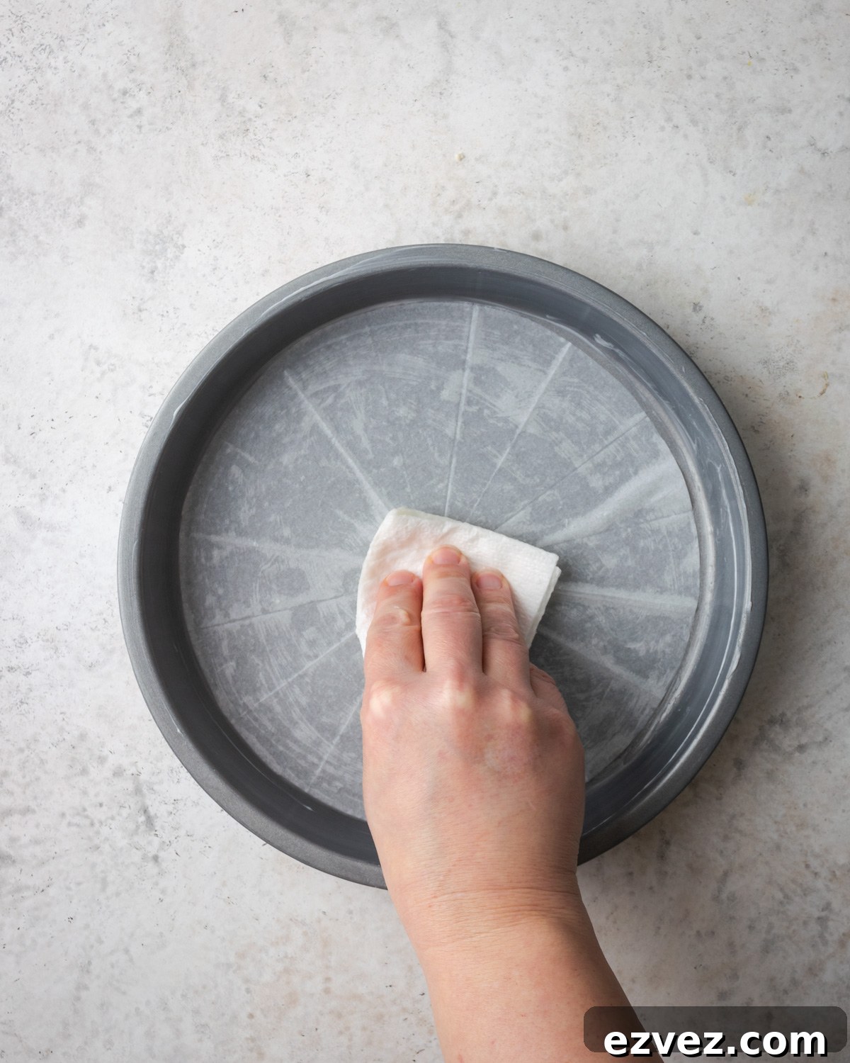 Rubbing grease on parchment paper inside of a round cake pan.