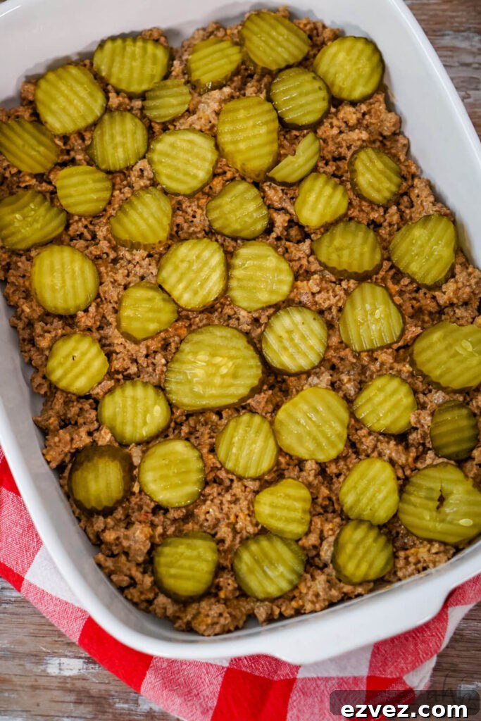 Big Mac Tater Tot Casserole Recipe: Cheesy Beef & Tots Bake 7 Browned ground beef is evenly spread in the bottom of a white baking dish. Pickle slices are evenly placed on top.