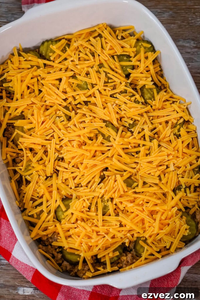 Big Mac Tater Tot Casserole Recipe: Cheesy Beef & Tots Bake 8 Ground beef and pickles are topped with shredded cheddar cheese in a white baking dish.