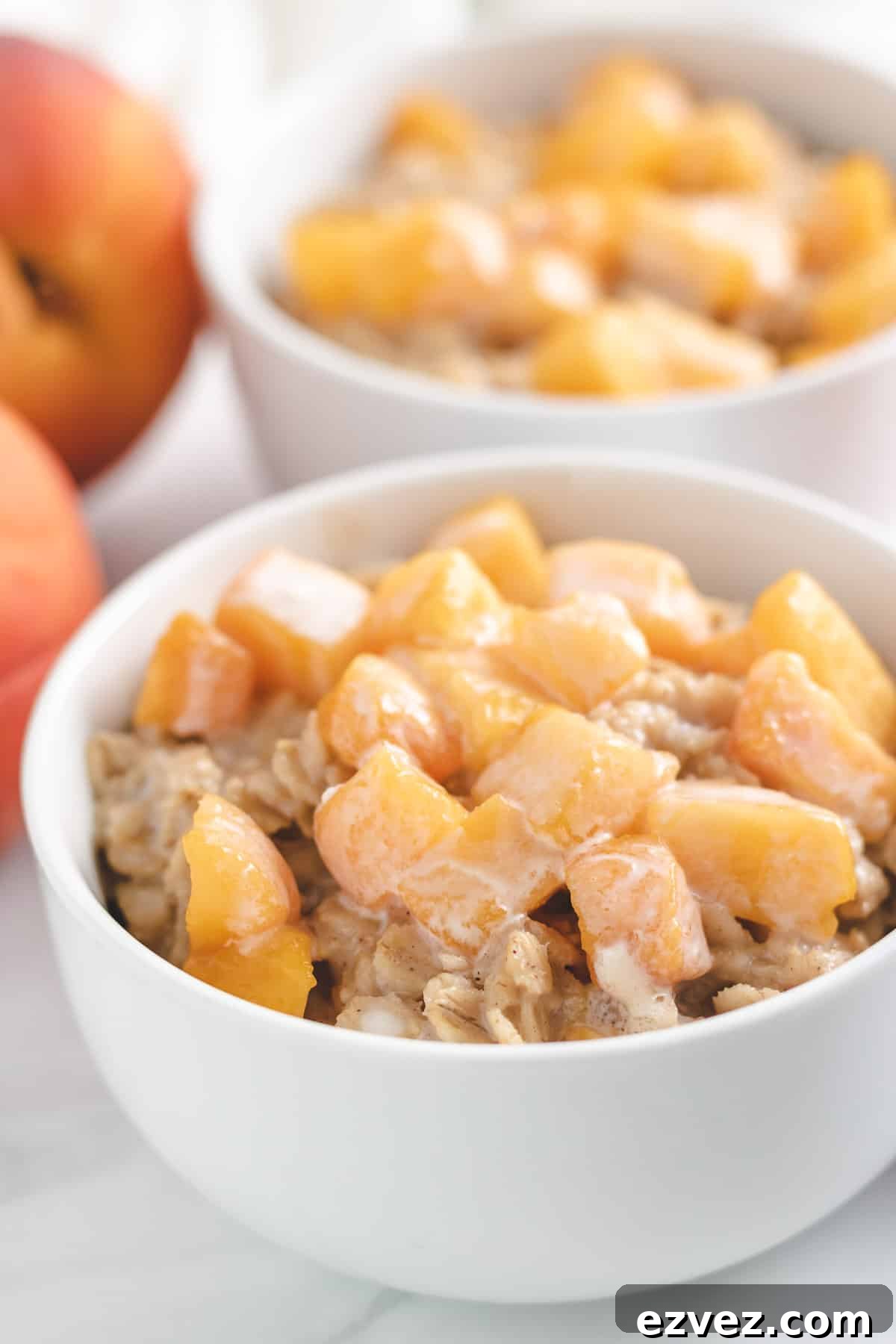 Close up view of oatmeal topped with peaches in a white bowl.