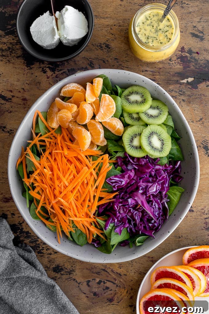 Ingredients to make Winter Salad arranged in a large bowl next to a jar of dressing and goat cheese.