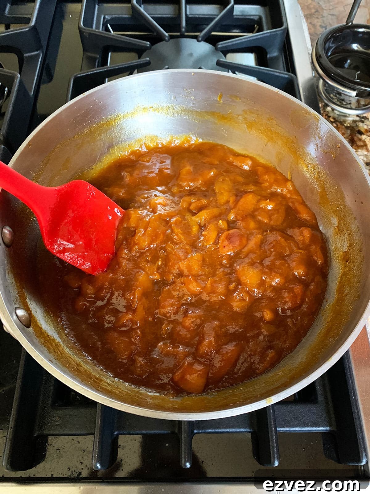 Apricot jam with brown sugar and bourbon cooked down in the pot on the stove with a red spatula.