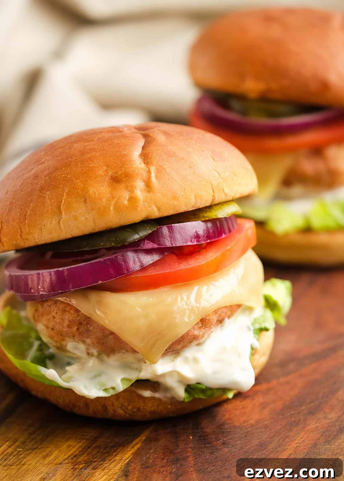 two turkey burgers with cheese, turkey, lettuce, mayonnaise, red onions, and pickles
