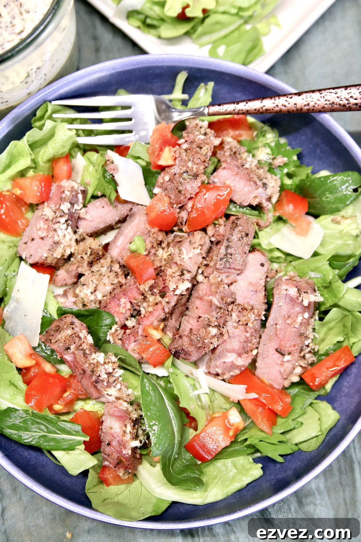 Bowl of salad topped with sliced steak.