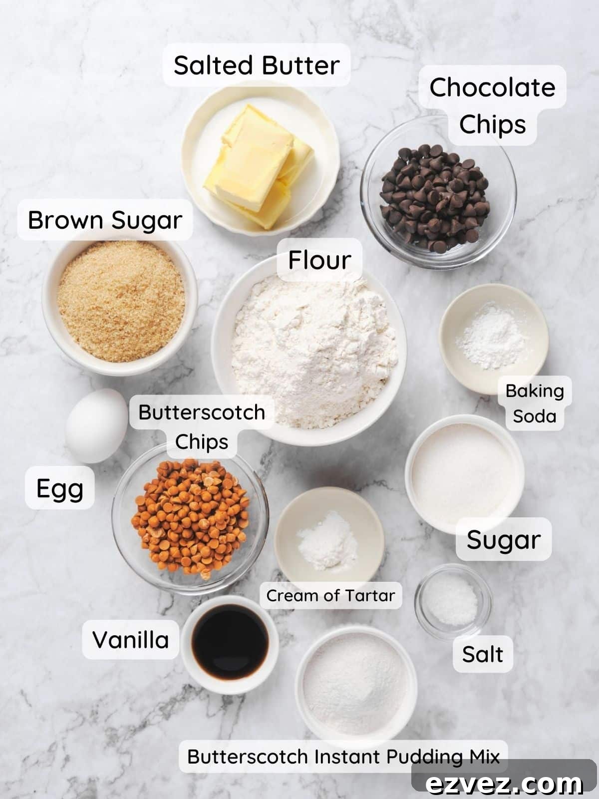 An overhead shot of chocolate chip butterscotch cookie ingredients with the text "flour, sugar, brown sugar, cream of tartar, baking soda, butterscotch chips, chocolate chips, vanilla, egg, butterscotch instant pudding mix, salted butter."